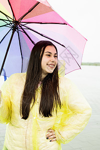 美丽的黑发美女 在雨中拿着多彩的雨伞女士喜悦下雨雨衣乐趣成人快乐公园微笑幸福图片