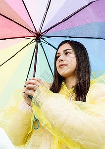 美丽的黑发美女 在雨中拿着多彩的雨伞天气彩虹雨衣喜悦微笑幸福乐趣季节女士下雨图片