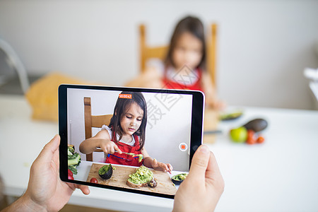 男性手与平板电脑记录 一个小女孩切鳄梨营养食物照片工具厨房孩子午餐成人砧板蔬菜图片