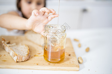 小女孩从一个罐子里摘蜂蜜 在一块面包旁边午餐营养糖浆勺子小吃砧板孩子早餐女孩小麦图片
