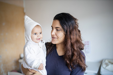 微笑的女人用白衣抱着她可爱的婴儿童年幸福兜帽家庭黑发卧室孩子父母母性母亲图片