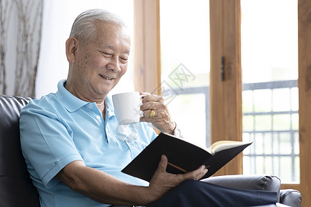 坐在沙发上 在客厅读有趣书的老人放松老年活动白色家庭生活乐趣家具知识头发智慧保险图片