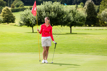 女性高尔夫手持高尔夫旗帜和俱乐部的肖像冒充推杆成功娱乐闲暇游戏课程运动草地阴影图片