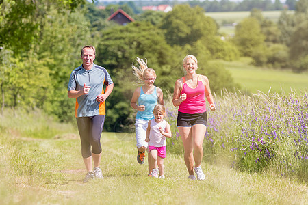 通过田间运动进行家庭运动父母女孩们场地有氧运动女士跑步运动装父亲女儿金发图片