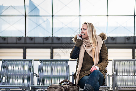 坐在板凳上用手机等待火车的女囚电话长椅女性火车站平台快车铁路运输城市旅行背景图片
