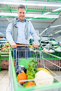 超市的人购物 用蔬菜推推他的电车乐趣部门杂货零售营养男人架子货架快乐产品图片
