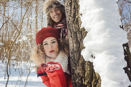 在雪中玩耍的情侣 躲在树干后面夫妻下雪喜悦男人丈夫季节合伙冬装幸福树木图片