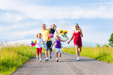 家庭在夏天奔下山丘爬坡太阳微笑国家孩子夫妻父母草地绿色跑步图片