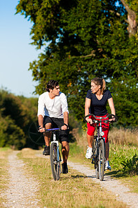 男人和女人用自行车运动天空活动骑术阳光照射乐趣训练男人闲暇草地慢跑者图片