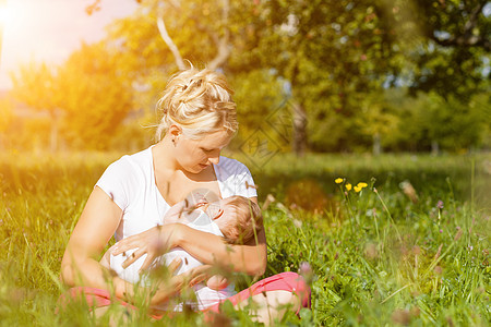 母亲在草地上喂育婴儿父母婴儿成人护理牛奶孩子花朵晴天妈妈母乳喂养图片