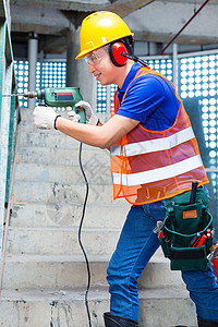 亚洲工人在建筑工地墙上钻井房子男人工匠钻孔楼梯机器安全帽耳朵听力头盔图片