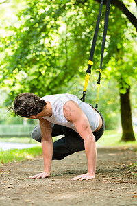 男子在城市公园做暂停训练教练运动男人弹力活动训练器训练师健康磁带悬吊培训师吊带图片