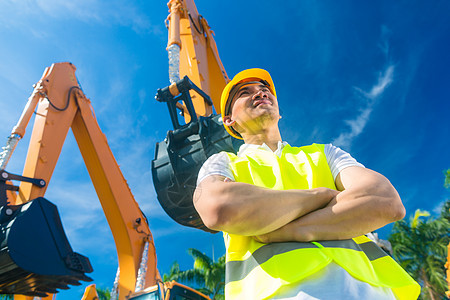 亚洲建筑工在铲挖土机前工业工人头盔挖掘机项目工程师毛虫男性导师职业图片