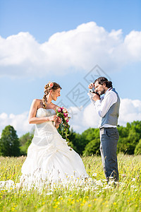夫妻在草地上拍照片新郎玫瑰妻子女士新娘相机结婚套装男人快乐图片