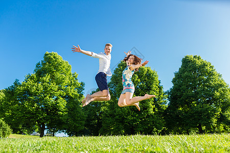 情侣在公园草坪上跳跃绿色喜悦假期草地女士友谊乐趣娱乐闲暇享受图片