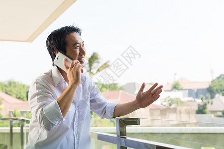 亚洲男子在阳台上用移动电话通过电话打电话手机城市人士商务细胞房子建筑学商业手掌图片