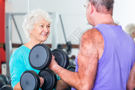 健身式举起哑铃的老年夫妇健身男人健身房女士中心活动锻炼微笑体操俱乐部背景图片
