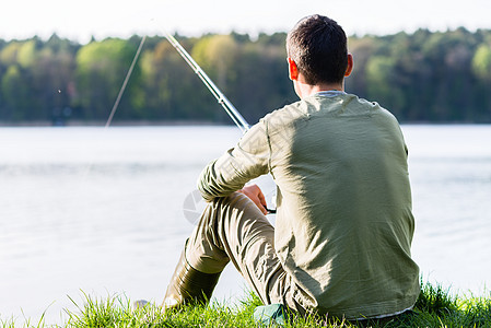 昂格勒坐在草地上 用他的棍子在湖边钓鱼凳子爱好男人运动闲暇河岸钓竿娱乐渔夫垂钓者图片