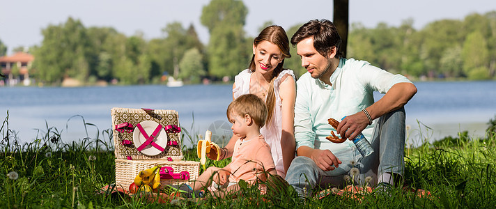 家庭在湖边野餐 坐在草地上爸爸男生食物男人微笑毯子儿子女士孩子太阳图片