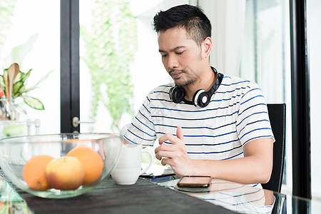 早餐时喝咖啡的印度尼西亚男人房子互联网水果药片平板咖啡冲浪电脑耳机橘子图片
