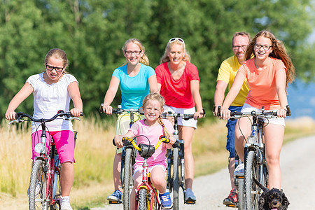 在泥土路上骑自行车的家庭团体骑术姐妹太阳父亲小路乐趣爸爸孩子们森林图片