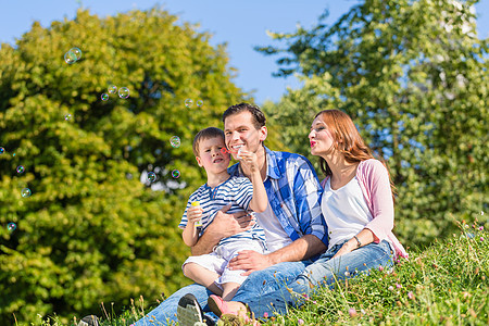 家庭坐在草地上玩肥皂泡男生丈夫父亲爸爸孩子女士男人树木幸福爬坡图片