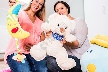 孕妇与朋友在预期的婴儿房中孩子微笑房间女性婴儿家庭教养妈妈公仔婴儿装图片