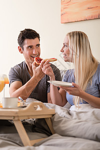 快乐的年轻夫妇在床上吃早餐面包卧室食物托盘眼镜男人果汁金发橙子妻子图片