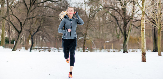 女人在冬天的公园里走过一条路慢跑鞋慢跑装闲暇树木白色运动小路耐力跑步微笑图片