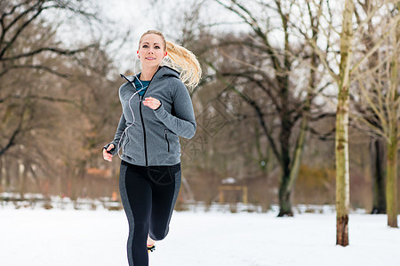 女人在冬天的公园里走过一条路乐趣跑步动机白色树木微笑运动训练慢跑鞋慢跑装图片