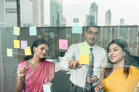 印度雇员在办公室玻璃墙上张贴催复提醒的警号成人建筑物团队女士次序职场反射城市男人项目图片