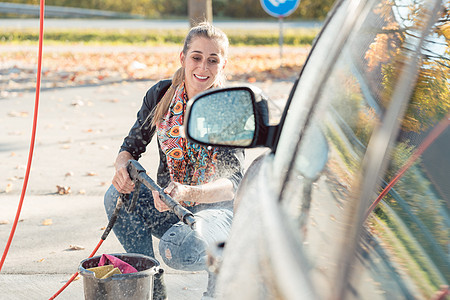 妇女用高压喷嘴清洗她的汽车软管洗车泡沫洗涤压力打扫自助洗涤剂肥皂商业图片