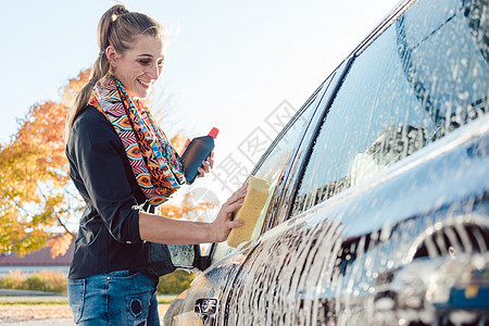 女性在她的汽车上泡泡泡沫洗涤剂压力刷子自助肥皂打扫海绵软管洗涤商业图片