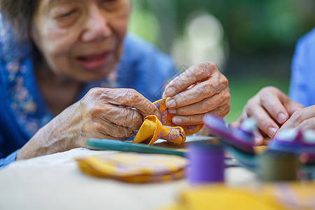 老年老年妇女在针头手工艺职业治疗中提供照顾者 治疗阿尔茨海默氏性痴呆症或痴呆症祖母衣服活动退休焦虑后院失智职业女士家庭图片