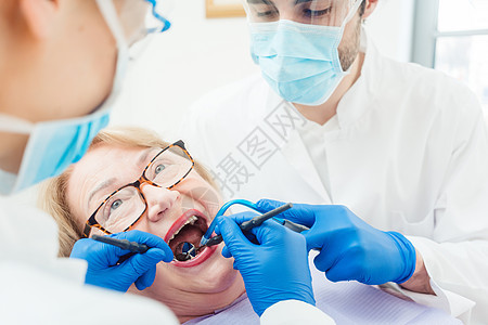 高级女病人治疗期间的牙科医生房间手术护目镜牙科女士防护服牙齿助手钻头诊所图片