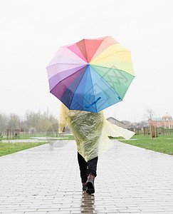 女人拿着多彩的伞 在雨中行走 从后面看图片