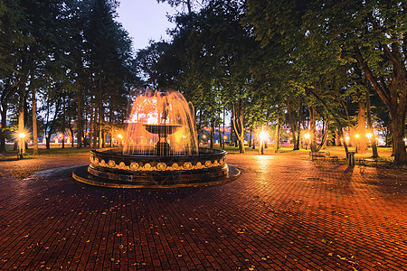 一个喷泉 在夜间公园里流着模糊的水流 灯光照亮 有石路 树木和长凳长椅照明正方形草地溪流景观场景灯笼城市胡同图片
