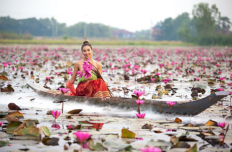 身着传统服饰的年轻亚洲女性在船上和池塘里的粉红色莲花 穿着传统服装的漂亮女孩 泰国语 大城府 优雅戏服历史金子女孩装饰品裙子寺庙图片