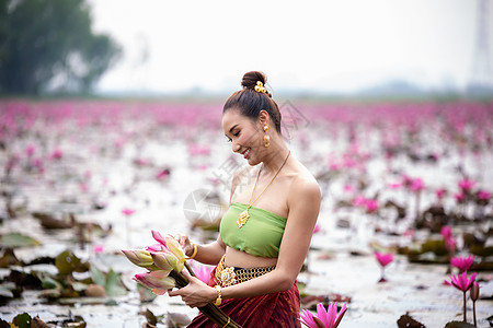 身着传统服饰的年轻亚洲女性在船上和池塘里的粉红色莲花 穿着传统服装的漂亮女孩 泰国语 大城府 优雅寺庙金子女孩佛教徒节日戏服装饰图片