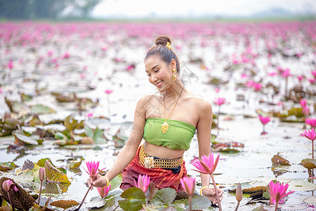 身着传统服饰的年轻亚洲女性在船上和池塘里的粉红色莲花 穿着传统服装的漂亮女孩 泰国语 大城府 优雅旅行戏服女孩女士文化裙子金子丝图片