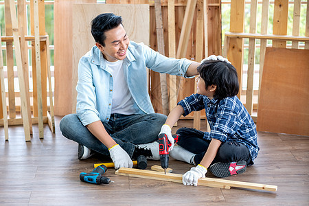 亚洲父亲在家庭木工工作场所钻木头时 心情愉快地摸着儿子的头 亚洲家庭观念留在家里 一起享受良好的关系爱好图片