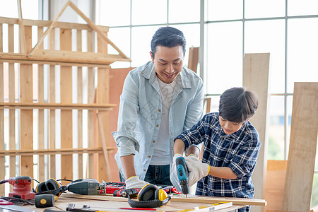 亚裔父亲教他的儿子使用电钻在家里做木工 在幸福家庭中与爱好或活动建立良好关系的概念木头男人木材木制品作坊工作钻头童年木匠工匠图片