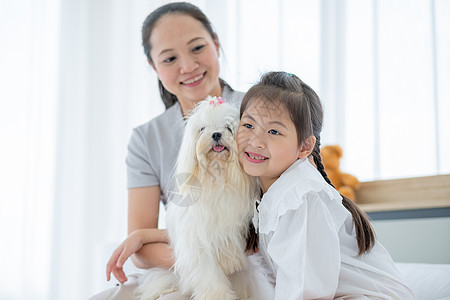 亚洲小女孩和白狗玩耍 坐在妈妈身边照顾卧室 幸福家庭的概念让人感到放松 可以和自己的宠物呆在家里童年小狗房子女士父母动物快乐母亲图片