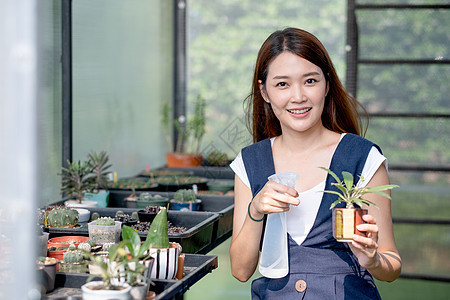 美丽的亚洲女孩拿着雾水瓶 喷洒水用小锅栽培 坐在她家的绿色花园里 种植仙人掌和其他植物概念是可持续的图片