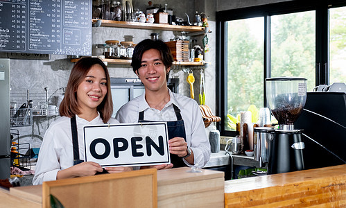 两个咖啡师或咖啡师男人和女人举着开放的旗帜 象征着准备在咖啡店为顾客服务 快乐与小企业合作和可持续发展的概念图片