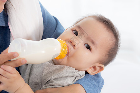 年轻的亚洲母亲在家里用奶瓶拥抱和喂养小女婴 新生儿的纯真与妈妈满意地喝酒 妈妈和孩子的关系和结合 家庭观念后代童年营养牛奶母性成图片
