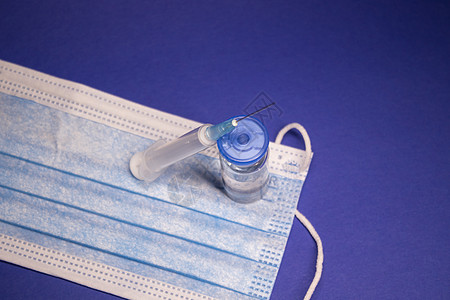 蓝色医用口罩上无标签的疫苗瓶和带注射针的医用注射器 在蓝色背景上隔离 治愈 冠状病毒疫苗 COVID19 的开发横幅肺炎科学药瓶图片