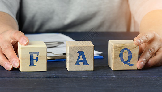 男性坐在一张桌子上 持有立方体 在蓝色背景的木块上输入 FAQ(经常询问的问题)图片
