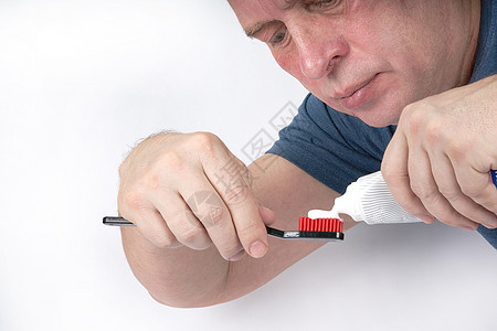 男人用红盾将牙膏挤压在黑牙刷上牙齿打扫口服卫生药品成人白色刷子医疗背景图片