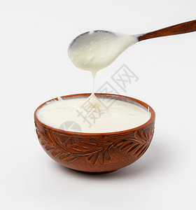 棕色陶瓷碗中的酸奶油和白底的木勺子图片